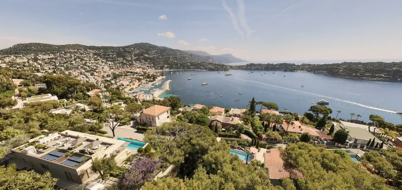 Vue en hauteur sur des constructions, des jardins et une baie côtière, illustrant un cadrage de contexte